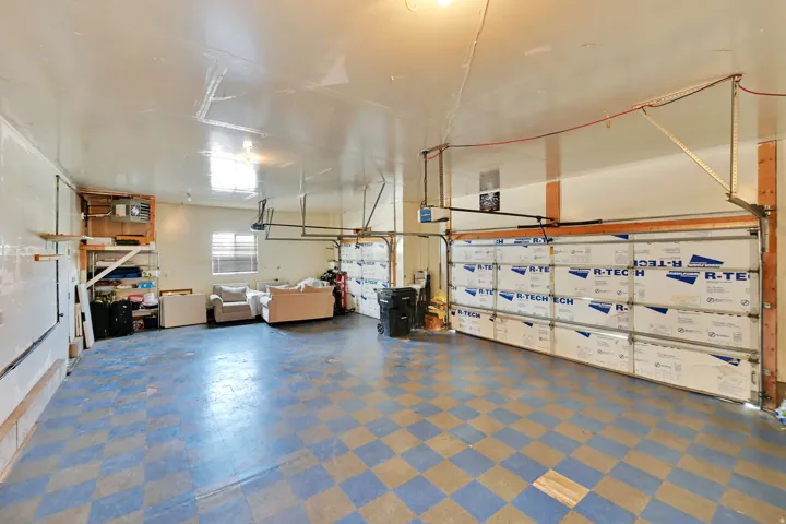 Spacious garage featuring two overhead doors, checkerboard flooring, built-in shelving, and a window for natural light