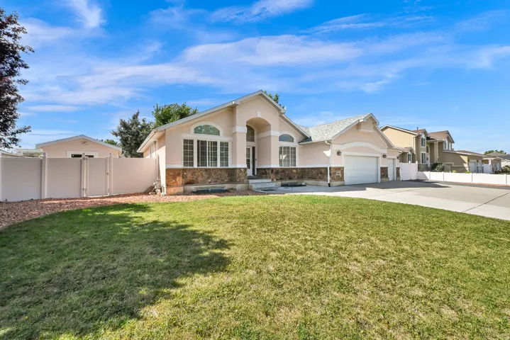 Single-story residence featuring a stucco exterior with stone accents, an attached garage, a front lawn, and a light-colored privacy fence