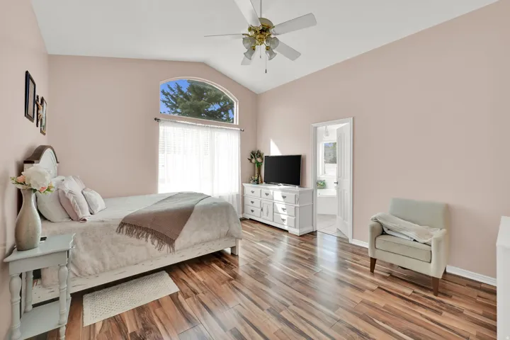 Vaulted ceiling with a ceiling fan, arched window, wood-finish flooring, and white interior door