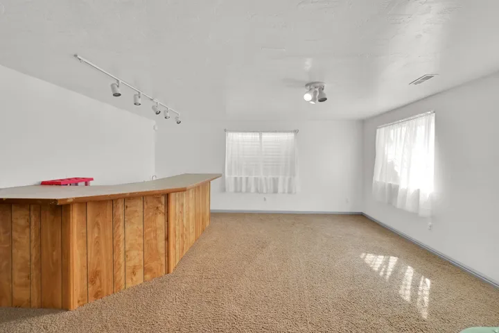 Built-in wood-paneled bar with a solid surface countertop, track lighting, and two windows