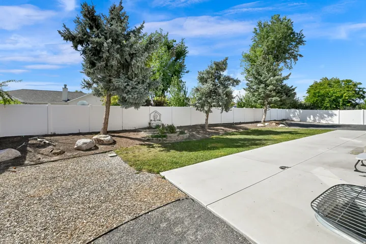 Manicured lawn with mature trees, a white perimeter fence, and a spacious concrete patio