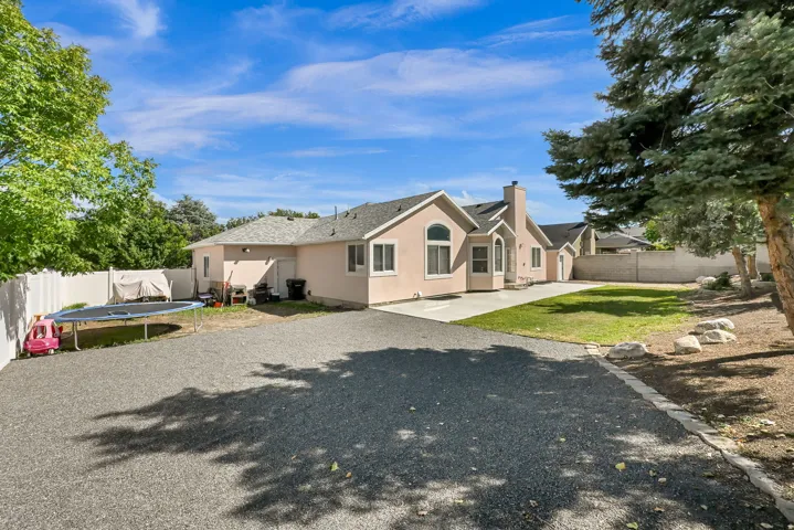 Stucco exterior with multiple windows, concrete patio, and a large gravel driveway