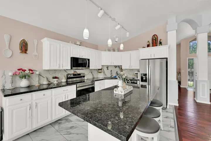 Galley kitchen with white cabinetry, black stone countertops, stainless steel appliances, and track lighting with pendant fixtures