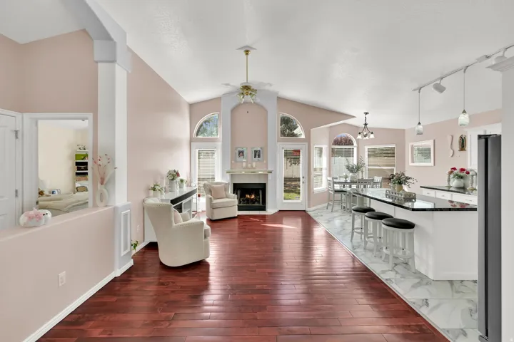 Vaulted ceilings, wood-finish flooring, a fireplace with a mantel, an eat-at kitchen island with a dark countertop, and a dining area with multiple windows