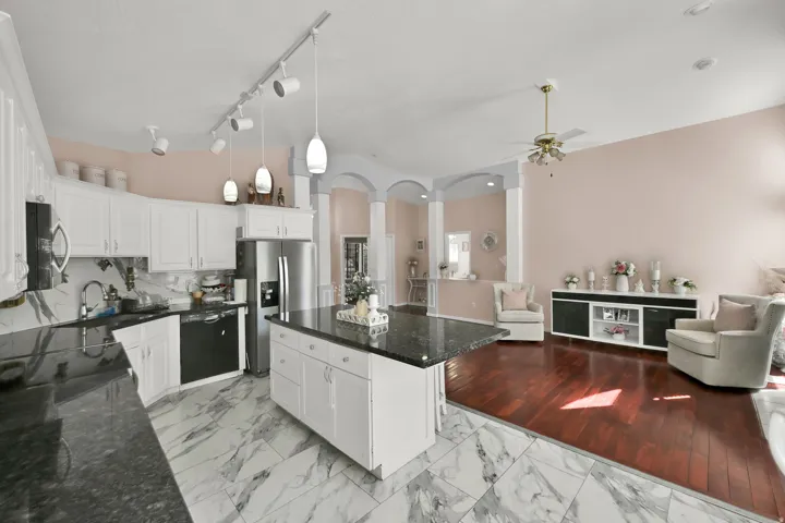White cabinetry kitchen with black countertops, stainless steel appliances, and marble-patterned tile flooring