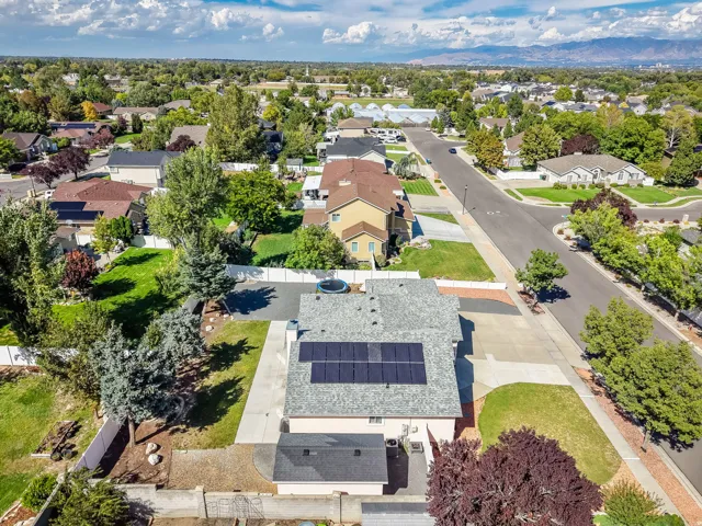Rooftop solar panels, shingle roofing, paved driveway, concrete walkways, and mature landscaping