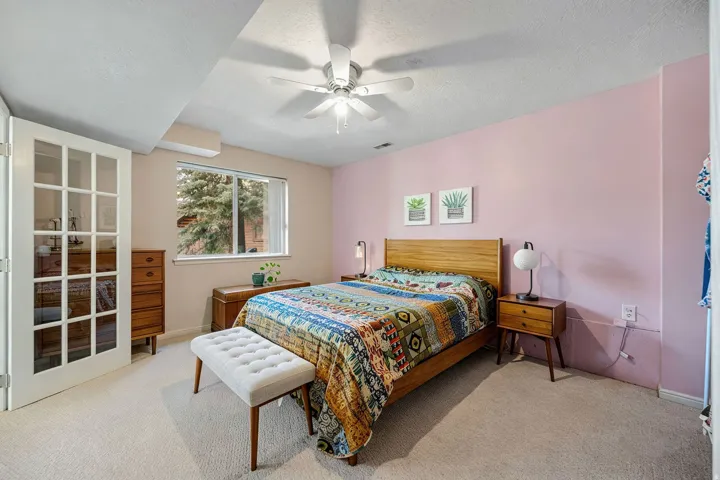 Large bedroom/room adjacent to the second living room on middle level. White French doors, window with exterior landscape, ceiling fan, carpet flooring, and a built-in wall unit