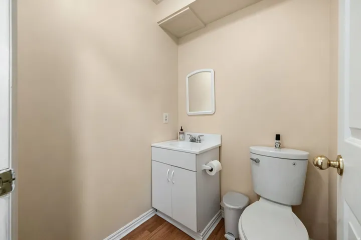 Middle level powder bath. Wood-finish flooring, white vanity with integrated sink, wall-mounted mirror, and a white toilet