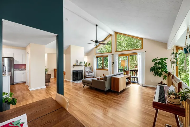 Vaulted ceiling with exposed beams, wood-finish flooring, floor-to-ceiling windows, and a wood-burning fireplace