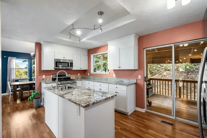 Kitchen featuring white cabinetry, granite countertops, stainless steel appliances, and wood-finish flooring