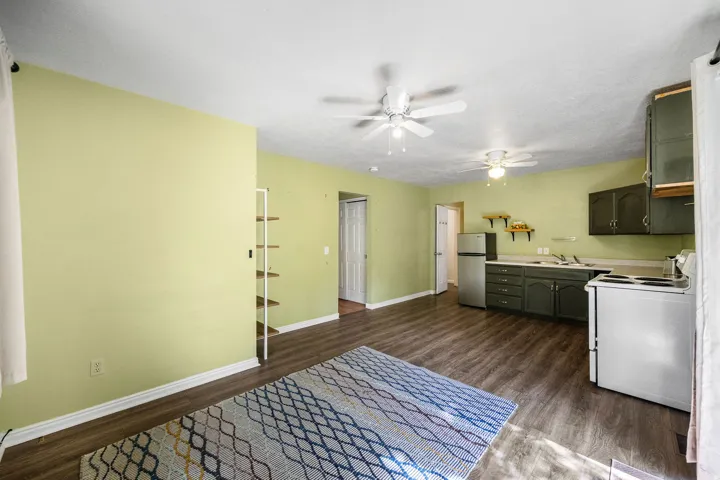 ADU Open-concept living area with wood-finish flooring, two ceiling fans, and a kitchen featuring dark-stained cabinetry, a stainless steel refrigerator, and a white electric range