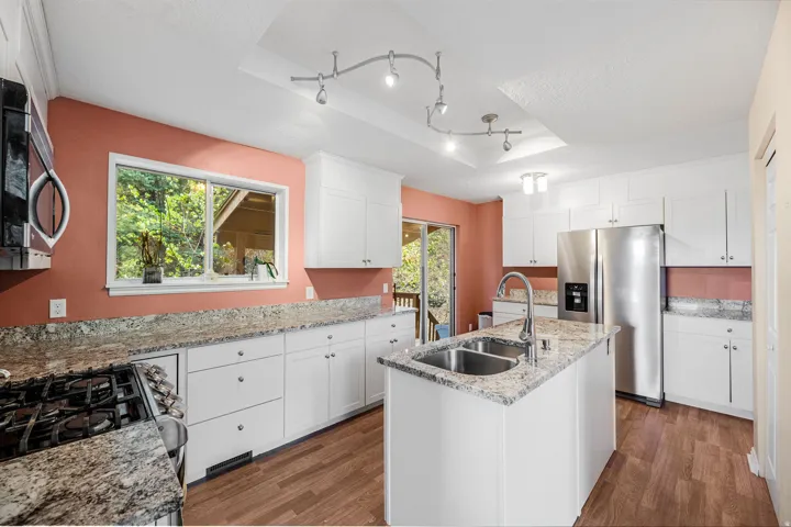 White shaker cabinetry, stone countertops, stainless steel appliances, wood-finish flooring, and recessed and track lighting
