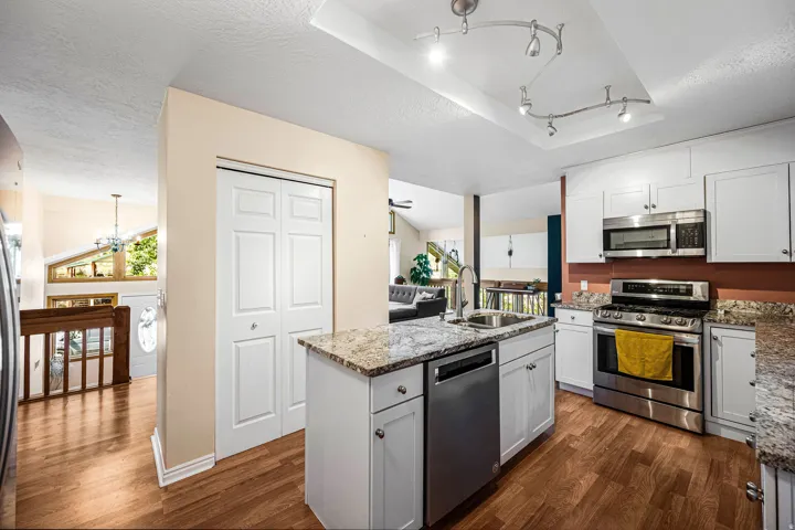 Kitchen featuring a central island with an integrated sink, granite countertops, white cabinetry, stainless steel appliances, and wood-finish flooring