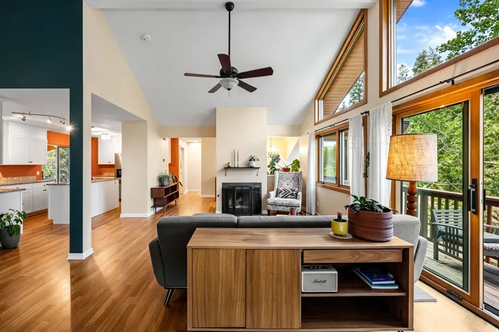 Vaulted ceilings, wood-finish flooring, a ceiling fan, a fireplace, and a glass sliding door leading to a deck