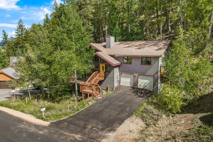 Multi-level residence featuring a pitched roof, wood-finish siding, two garage doors, and a wood deck with stairs