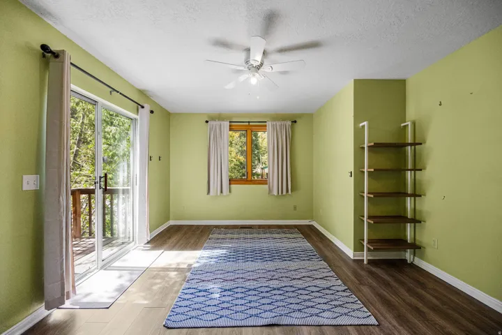 Wood-finish flooring with a ceiling fan, a sliding glass door, an additional window, and built-in shelving