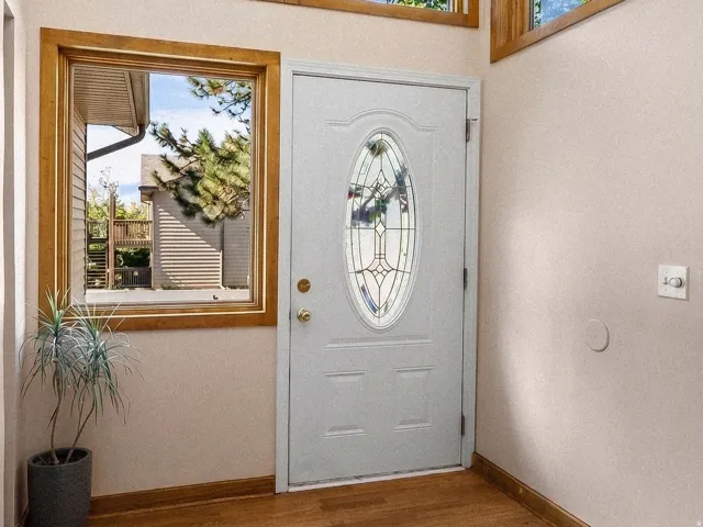 Entryway featuring a white door with decorative glass inlay, wood-finish flooring, and multiple geometric windows with wood trim