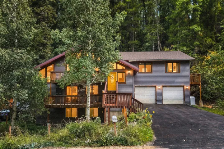 Multi-level residence featuring gray siding, a prominent wood deck, and a two-car garage