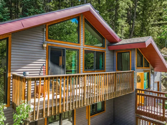 Multi-level exterior with wood-finish siding, A-frame architecture, extensive window placement, and a wood balcony with railing