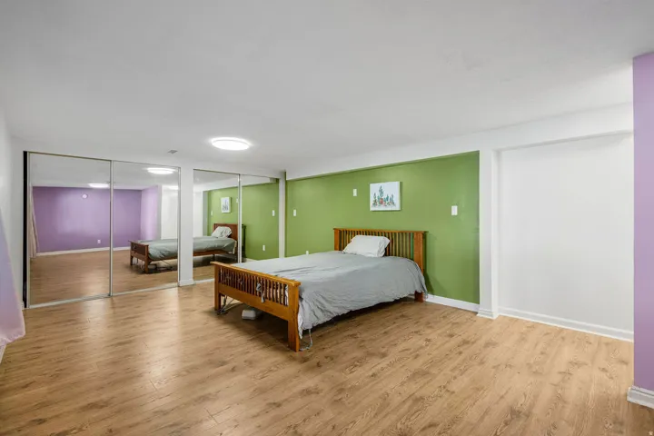 Wood-finish flooring, mirrored sliding closet doors, ceiling-mounted lighting, and a neutral ceiling