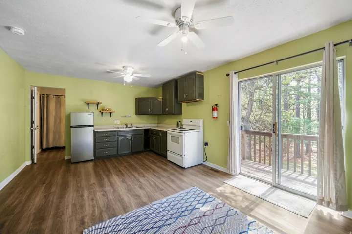 Wood-finish flooring, ceiling fan, white appliances, and sliding glass door to an outdoor deck with wood railings