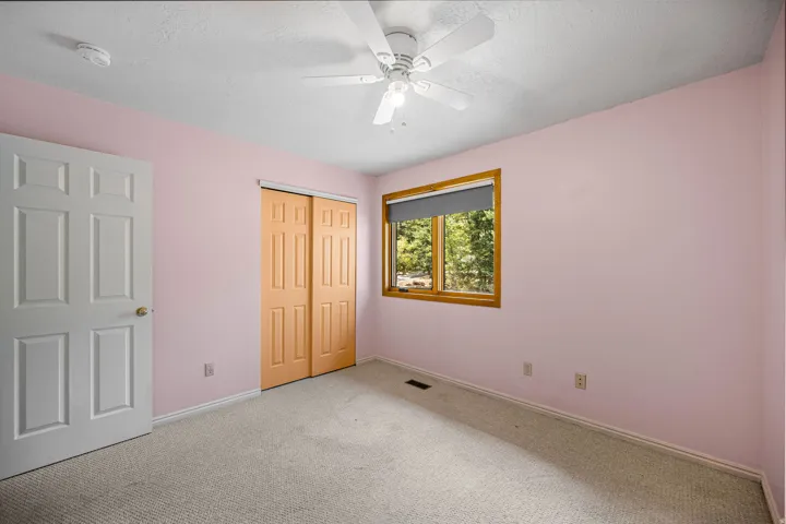 Ceiling fan fixture, wood-framed window, carpeted flooring, paneled interior door, and bi-fold closet doors