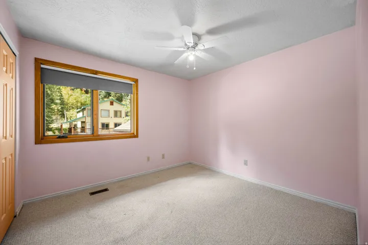 ADU second bedroom adjacent to the living room. Window with wood trim, ceiling fan, carpet flooring, and light-colored walls