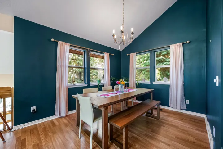 Vaulted ceiling with a chandelier, wood-finish flooring, and two large windows