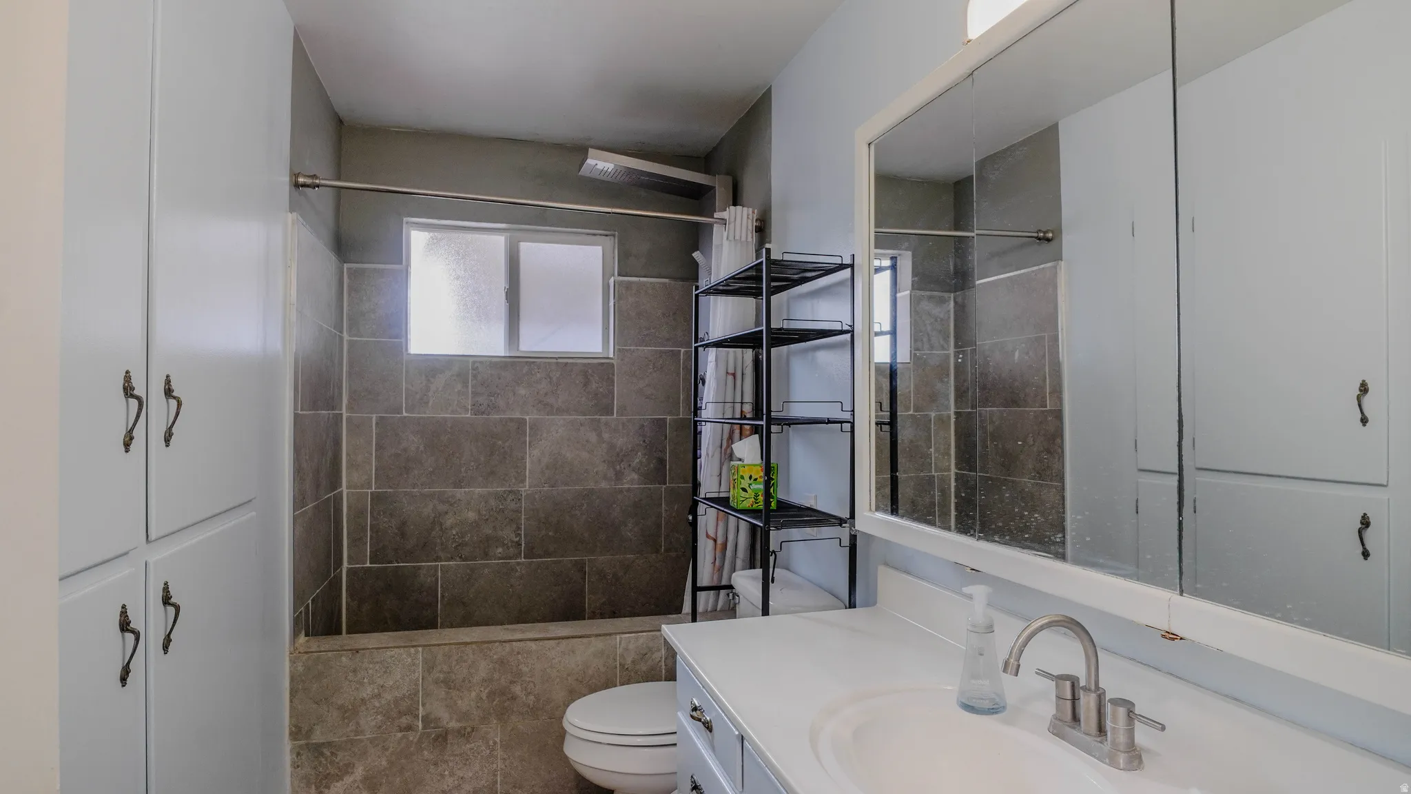 Bathtub with tiled surround, frosted window, built-in storage cabinetry, vanity with integrated sink, and large wall-mounted mirror