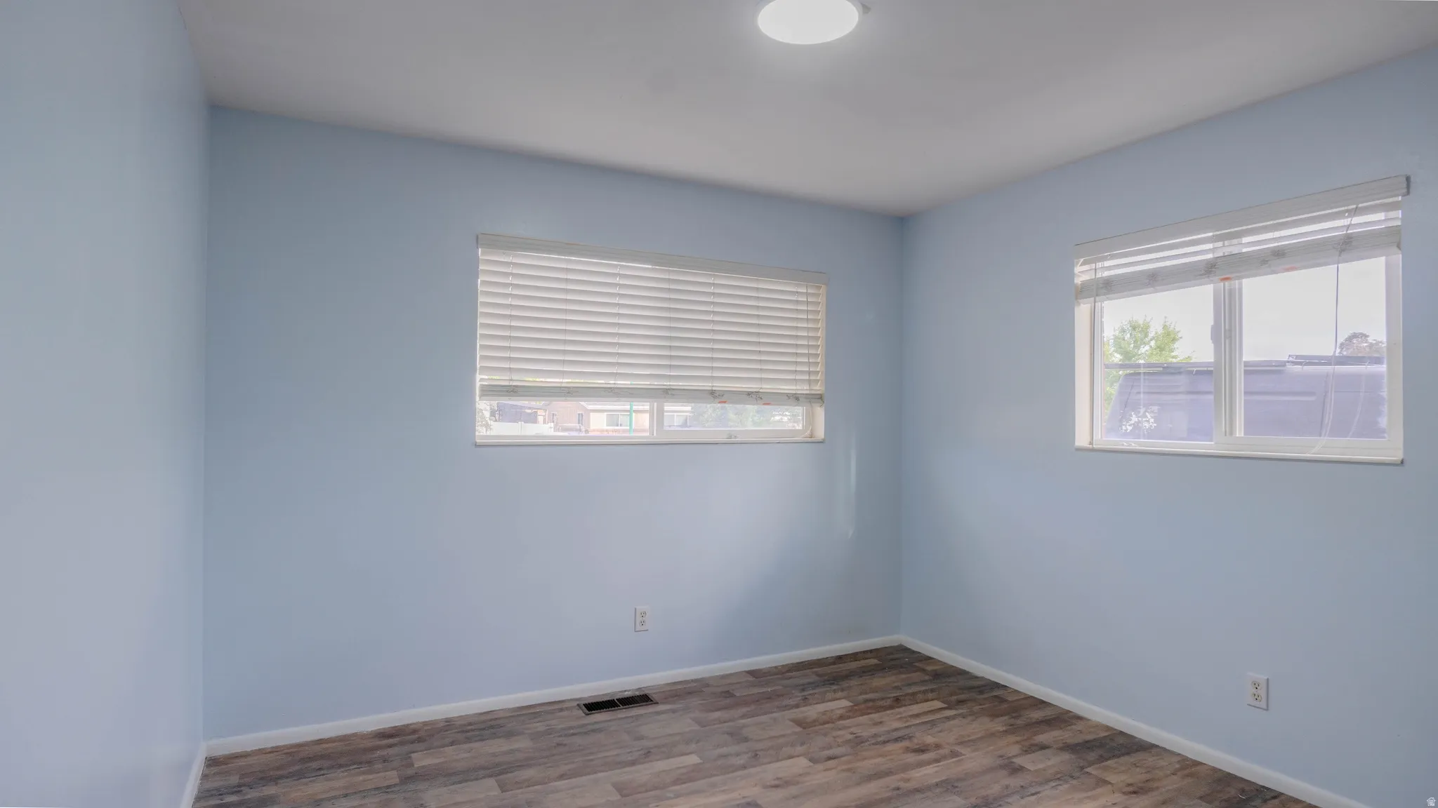 Wood-finish flooring, light blue walls, and two windows with blinds