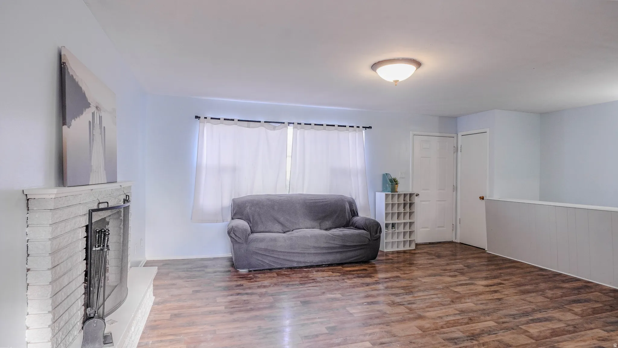 Brick fireplace with a hearth, wood-finish flooring, white paneled wall, and a flush mount ceiling light