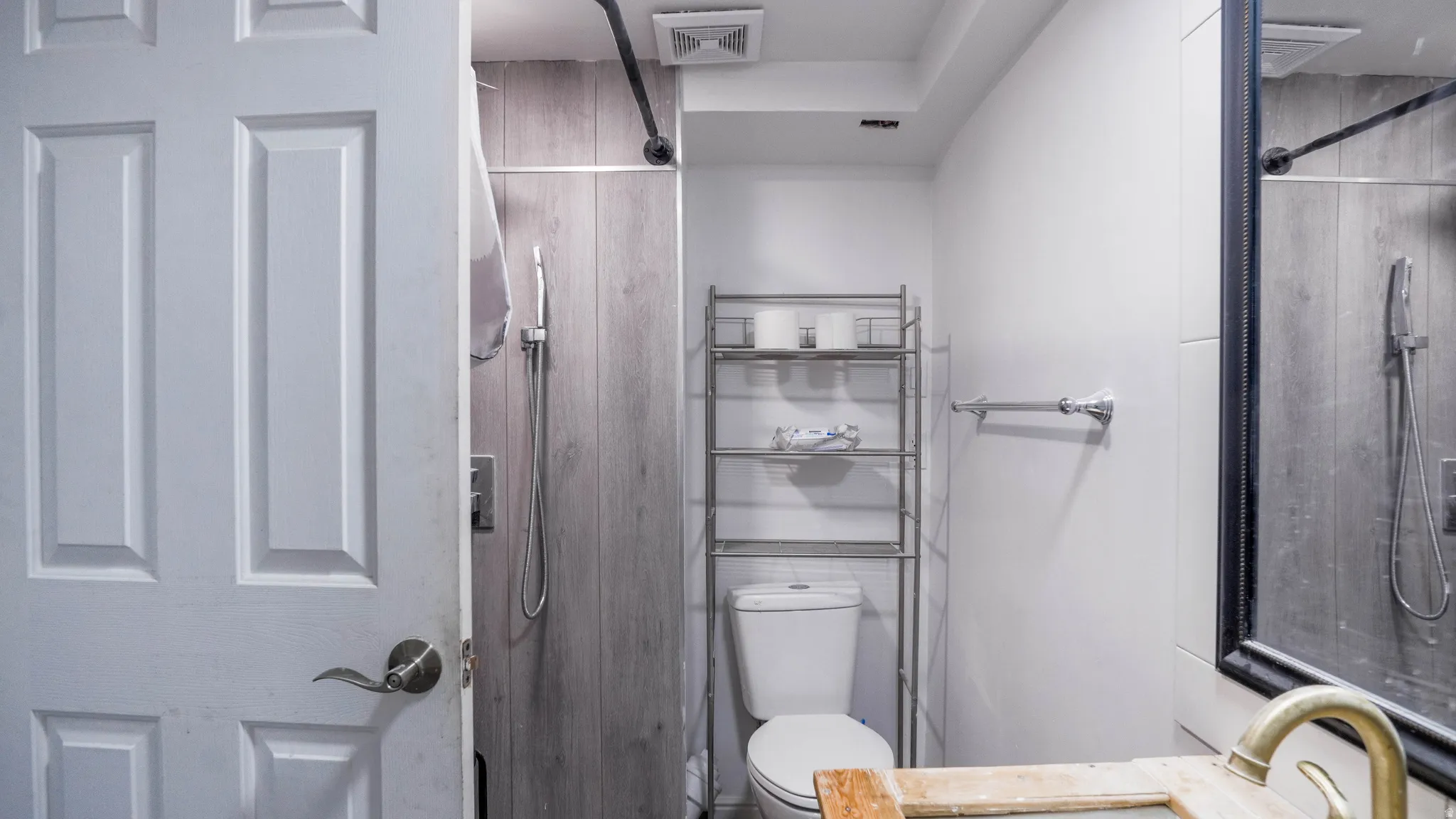 Modern bathroom featuring a wood-look shower surround, white toilet, and a vanity with a brass-finish faucet