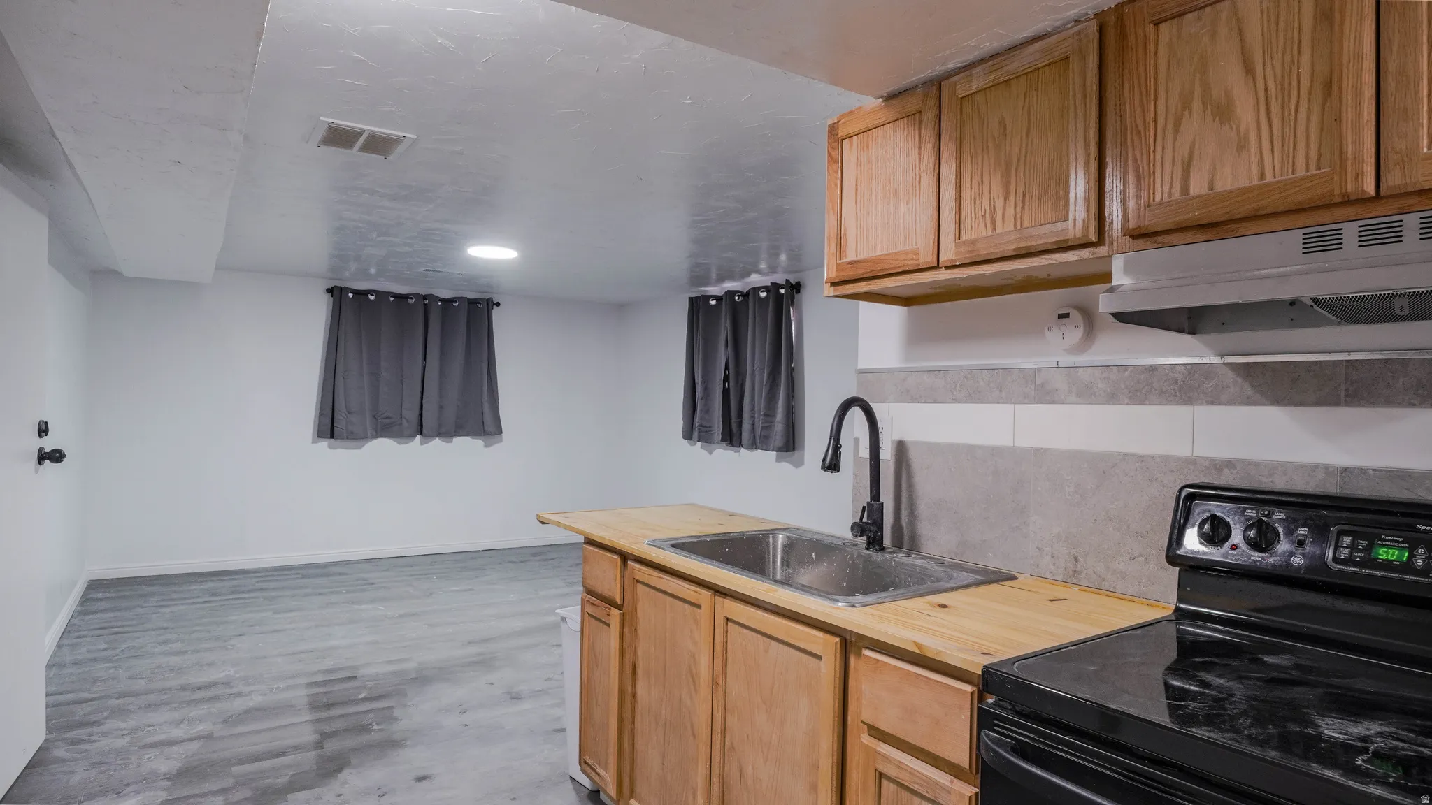 Kitchenette with wood cabinetry, wood-finish countertops, stainless steel sink with a matte black faucet, and a black electric range