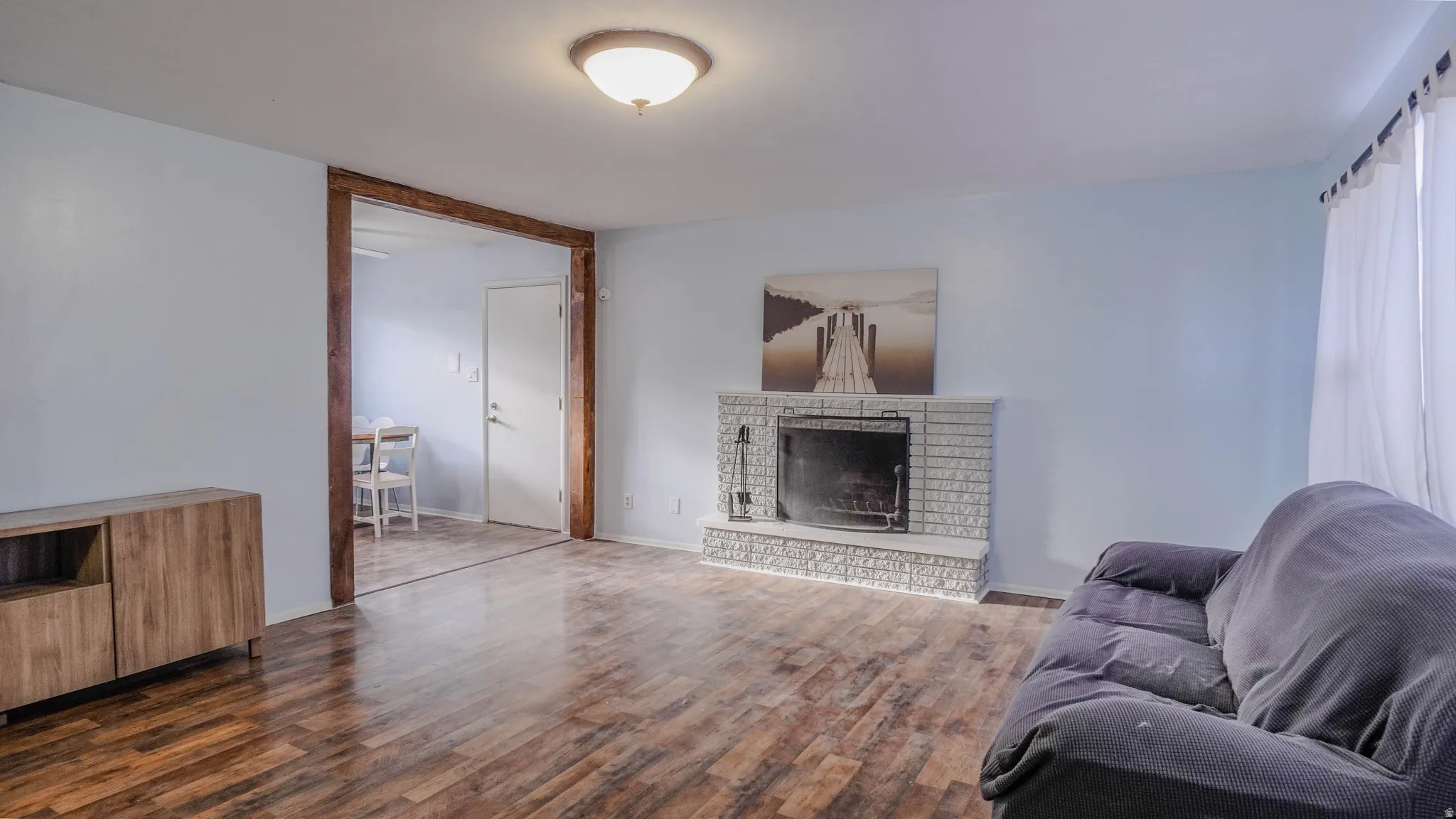 Wood-finish flooring throughout, brick fireplace with a black firebox, recessed lighting, and a wide cased opening with wood trim