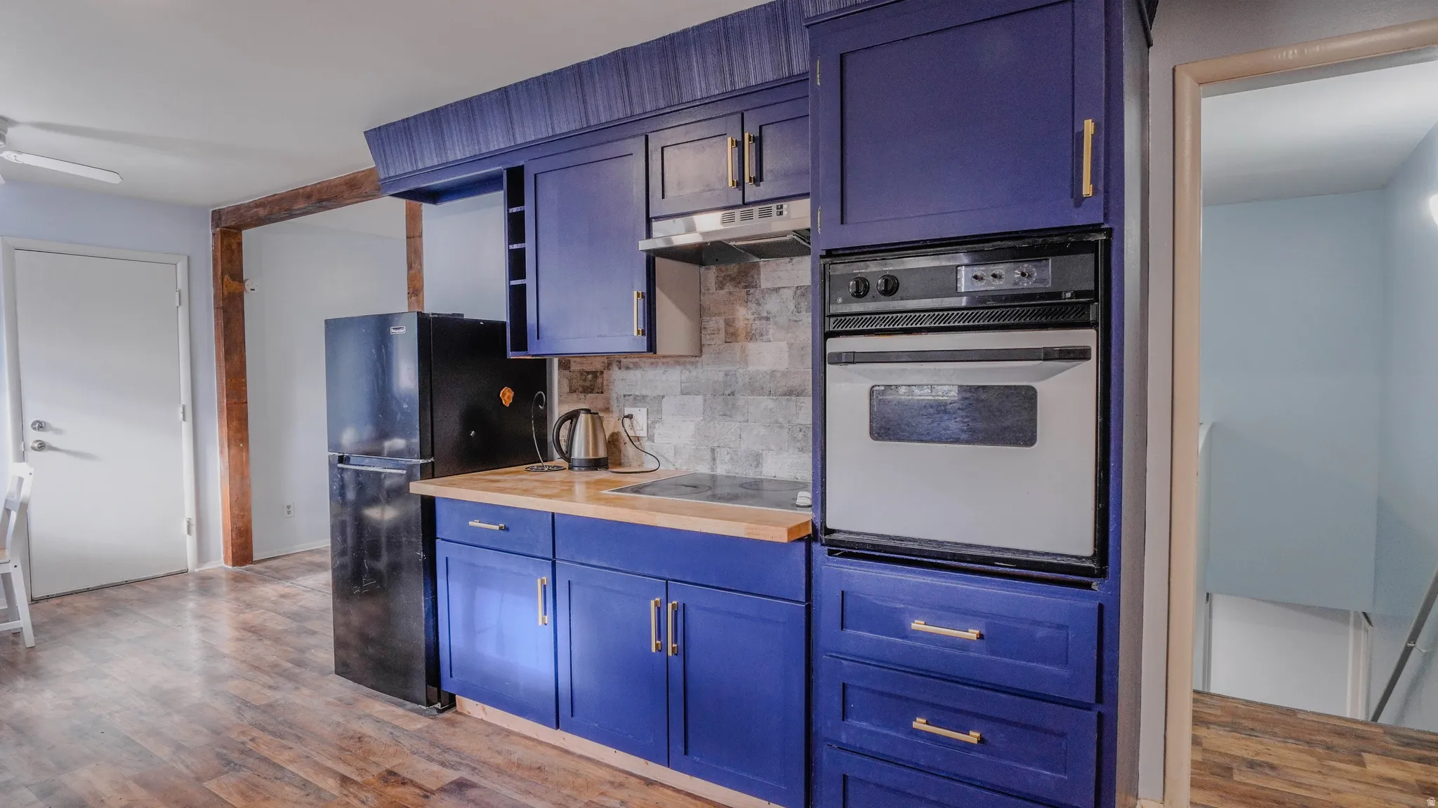 Kitchen featuring blue cabinetry with gold-finish hardware, built-in oven, wood-finish countertops, and wood-finish flooring