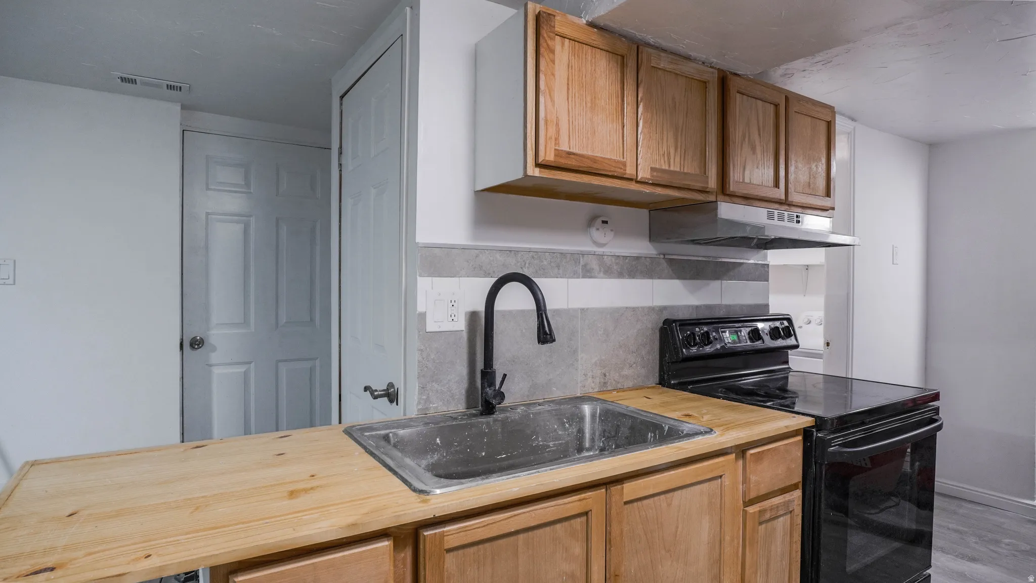 Kitchenette featuring wood-finish cabinetry, stainless steel sink with matte black faucet, electric range, and range hood