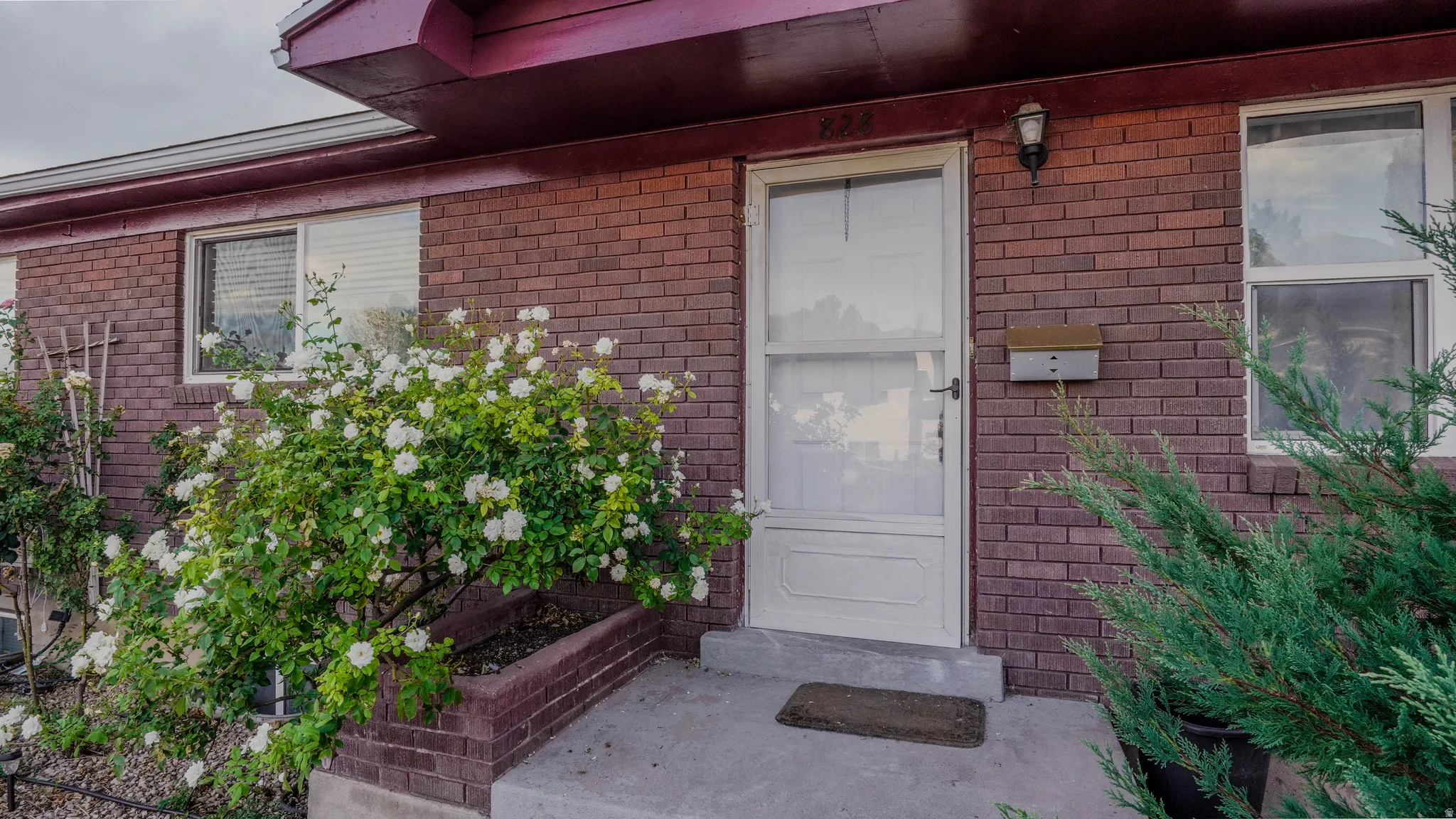 Brick exterior with a white storm door, an exterior wall light fixture, and a built-in mailbox