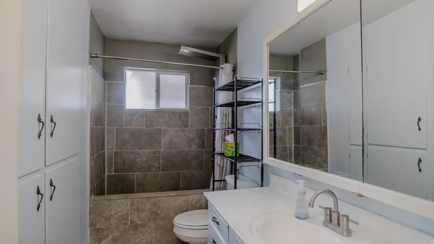 Bathtub with tiled surround, frosted window, built-in storage cabinetry, vanity with integrated sink, and large wall-mounted mirror