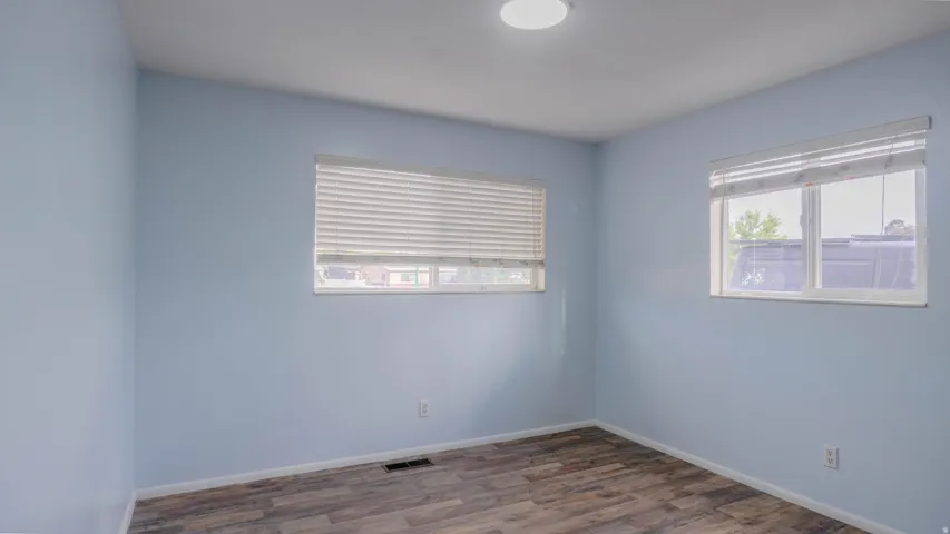 Wood-finish flooring, light blue walls, and two windows with blinds