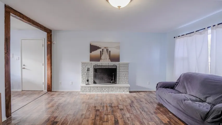 Wood-finish flooring throughout, white painted brick fireplace with hearth, and a white ceiling-mounted light fixture