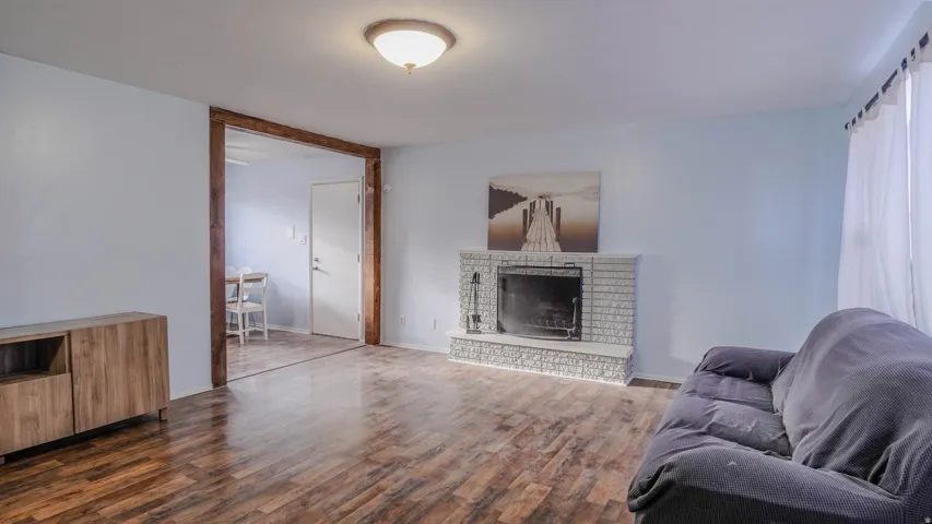 Wood-finish flooring throughout, brick fireplace with a black firebox, recessed lighting, and a wide cased opening with wood trim
