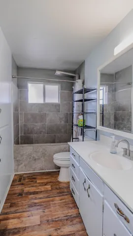 Wood-finish flooring, white vanity with integrated sink, white countertop, white built-in cabinetry, and tiled shower surround with tub