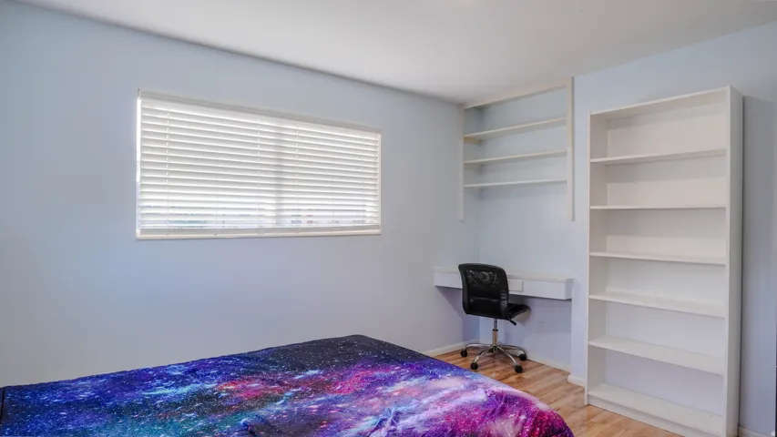 Built-in shelving, integrated desk, window with blinds, and wood-finish flooring