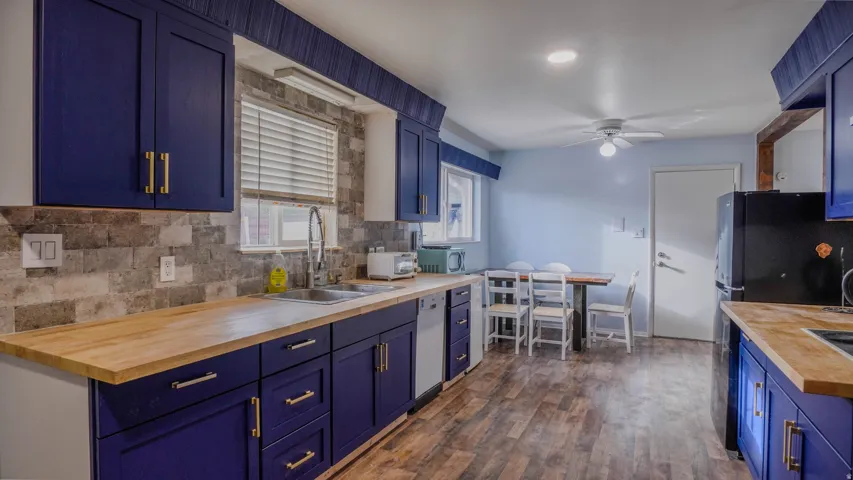 Blue cabinetry with brass-finish hardware, wood-finish countertops, stainless steel sink with a high-arc faucet, and a stone-finish backsplash