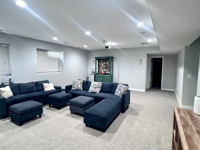 Recessed lighting, light gray walls, light gray patterned carpeting, built-in display cabinet, and window with blinds