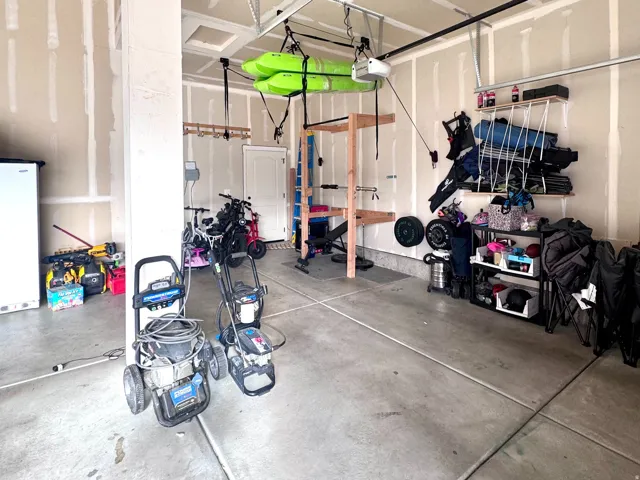 Concrete flooring with expansion joints, unfinished walls, and an overhead garage door opener system