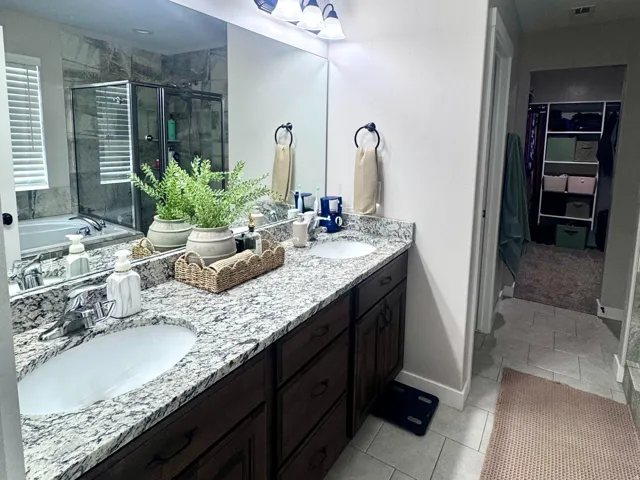 Double vanity with granite countertops, undermount sinks, dark wood cabinetry, and overhead sconce lighting