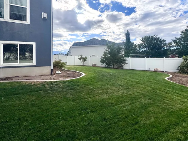 Expansive grassy yard with a white privacy fence and curved landscaping beds