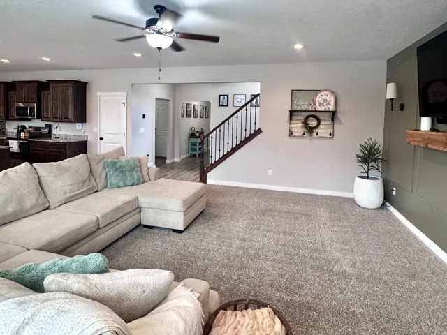 Recessed lighting, wood-finish ceiling fan, neutral carpeting, and a built-in wooden mantel