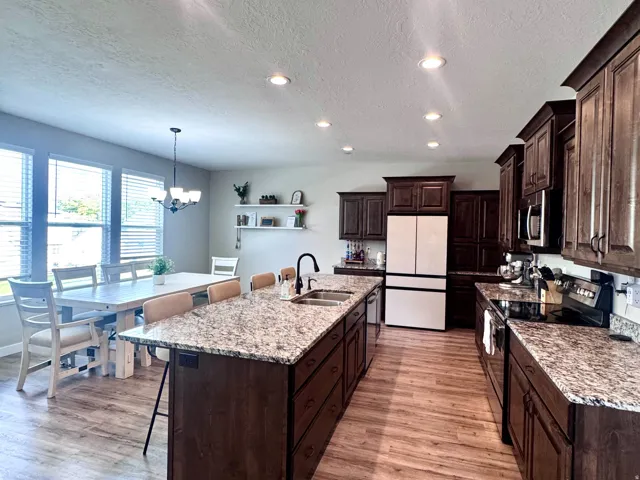 Kitchen featuring wood-finish flooring, dark wood cabinetry, light speckled countertops, a large island with seating, and recessed lighting